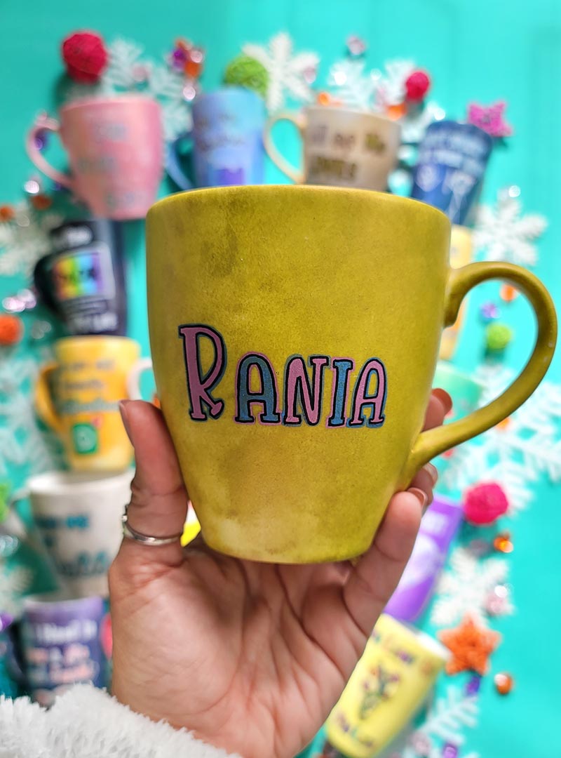 A hand-painted greenish bronze mug with the name "Rania"