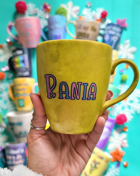 A hand-painted greenish bronze mug with the name "Rania"