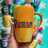 A yellow orange hand-painted mug with the name 