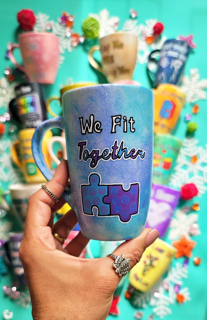 A hand-painted  light blue purple mug with the words "we fit together" and then below it a painting of two puzzle pieces perfectly fitting together