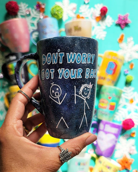 A hand painted black galaxy mug with the words "don't worry, I got your back " and a drawing of 2 stick figures with the girl holding the back of the boy