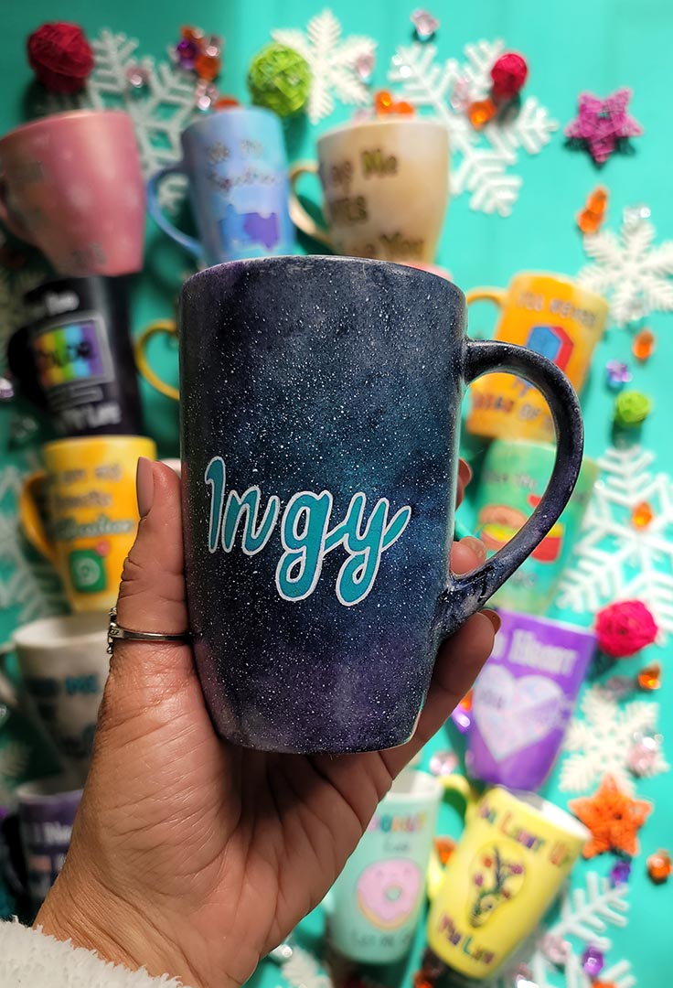 A hand painted black galaxy mug with the name "ingy"