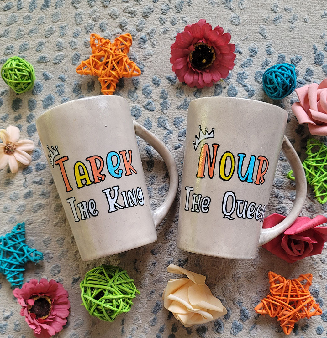 2 hand-painted taupe mugs, one with the words "Tarek the king" and the other with the words "Nour the queen"