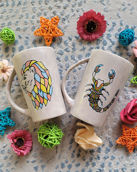 2 hand-painted taupe mugs one with the leo zodiac sign and the other with the scorpio zodiac sign