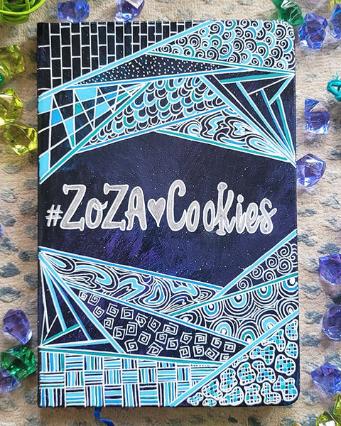 A Bluish galaxy hand painted notebook with patterns on the top and bottom and the words "Zoza heart Cookies" is written