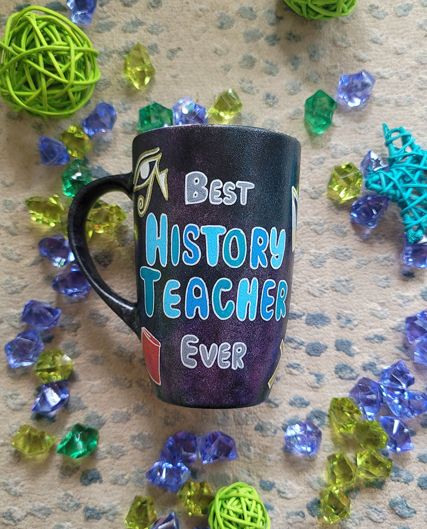 A Black Sky Hand painted mug with the words "Best History teacher Ever" and Egyptian history icons scattered all over