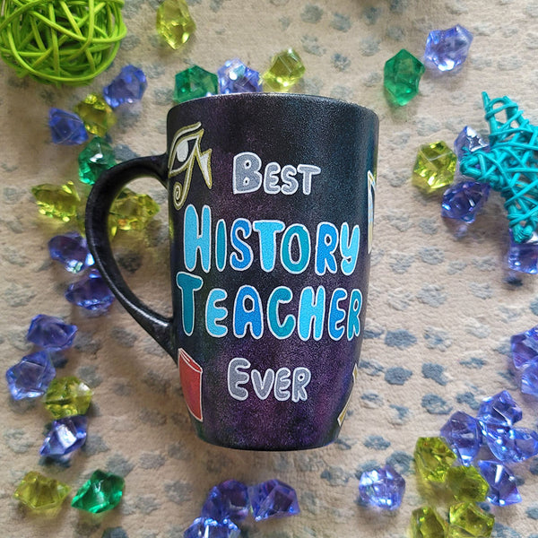 A Black Sky Hand painted mug with the words "Best History teacher Ever" and Egyptian history icons scattered all over