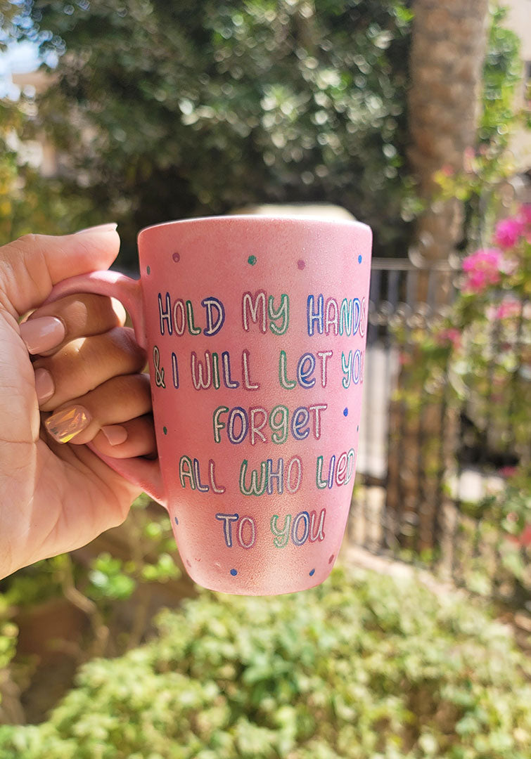 A hand-painted shimmery pink mug with the words "Hold my hand and I will Let you forget all who lied to you"