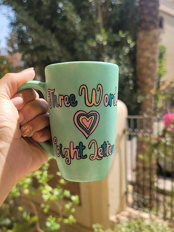 A Hand painted green Mug with the words "three words, Eight Letters" written and a heart place in between the two sentences