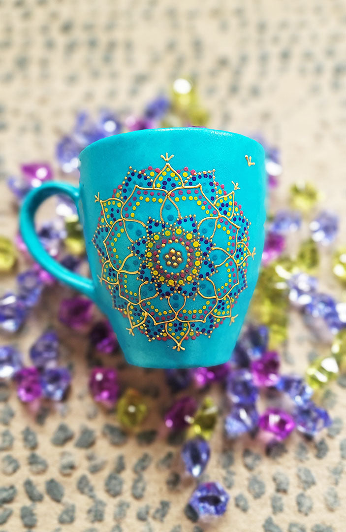 A hand painted blue Indian color mug with a mandala painted in gold