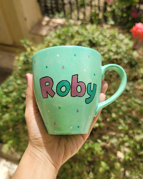 A mint Colored mug with the name "Roby" with white and green dots and pink stars scattered all over