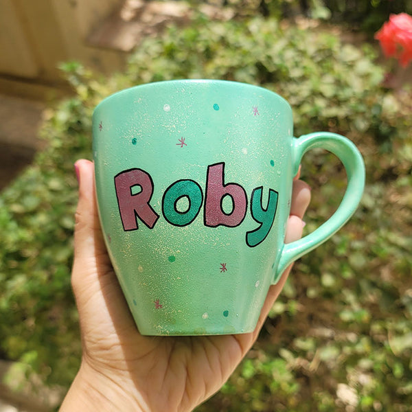 A mint Colored mug with the name "Roby" with white and green dots and pink stars scattered all over