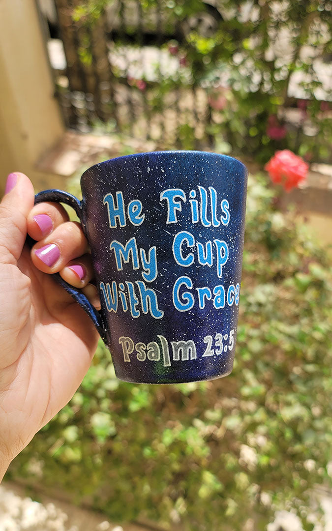 a Bluish galaxy hand painted mug with the words "He fills my cup with grace" Pslam 23:5