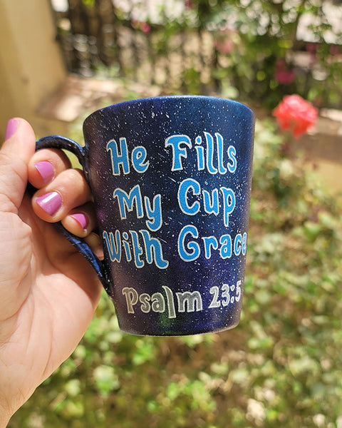 a Bluish galaxy hand painted mug with the words "He fills my cup with grace" Pslam 23:5