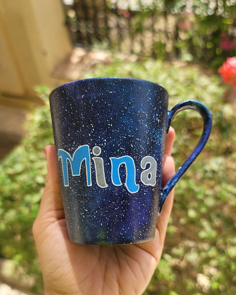 a Bluish galaxy hand painted mug with the name "mina"