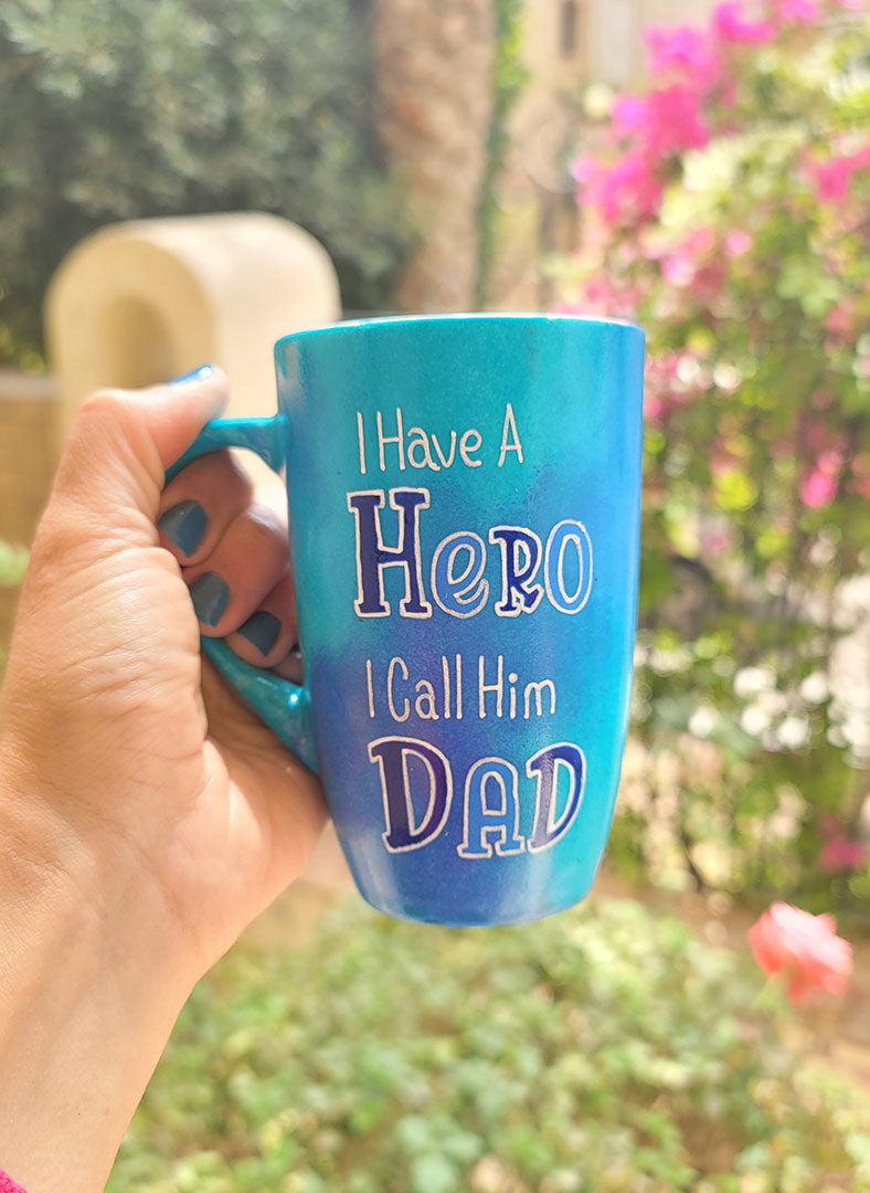 A blue handpainted mug with the words "I Have a Hero. I Call Him Dad" and the words Hero and Dad are in larger font and colored