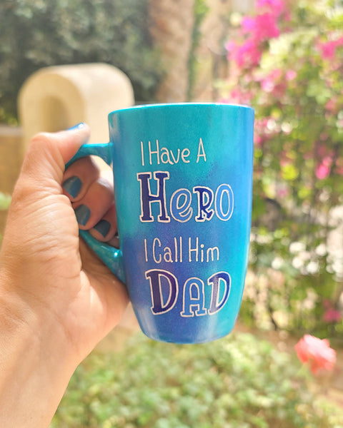 A blue handpainted mug with the words "I Have a Hero. I Call Him Dad" and the words Hero and Dad are in larger font and colored