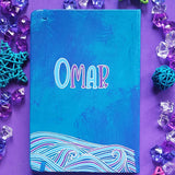 A Blue Hand painted notebook with patterns of waves drawn in the bottom and the name 