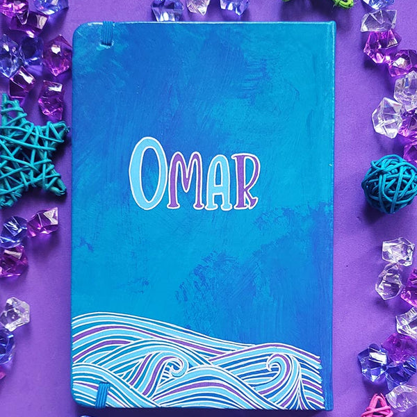 A Blue Hand painted notebook with patterns of waves drawn in the bottom and the name "Omar""