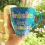 A blue hand painted mug with the words "Nermine Serry, worlds beautiest princess" and colorful dots scattered all over