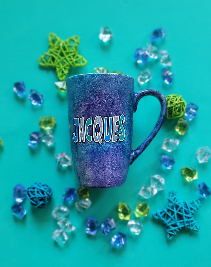 A bluish galaxy hand painted mug with the name "Jacques"