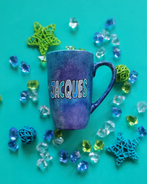 A bluish galaxy hand painted mug with the name "Jacques"