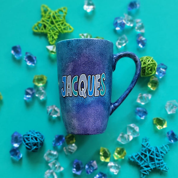 A bluish galaxy hand painted mug with the name "Jacques"