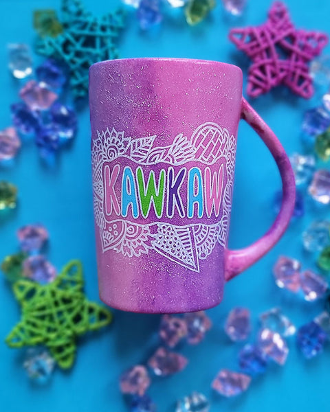 A pink galaxy hand painted mug with the name "kawkaw" inside a cloud of doodles