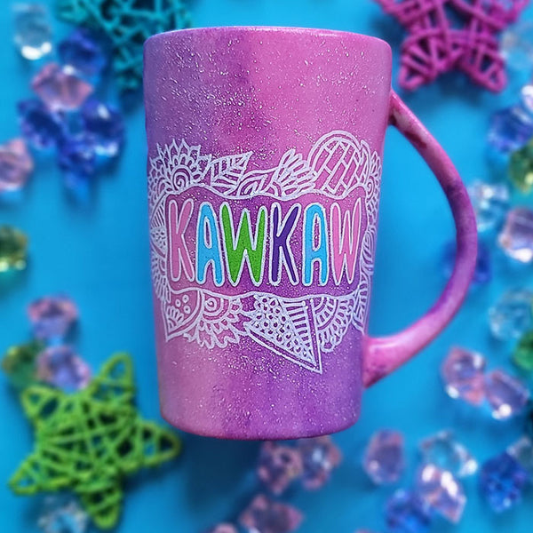 A pink galaxy hand painted mug with the name "kawkaw" inside a cloud of doodles