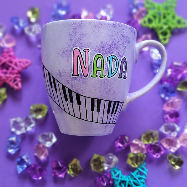 A Lilac hand painted mug with the name nada and piano buttons drawn diagonally on the mug