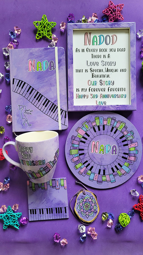 A Gift Set containing matching mug, notebook, frame,mdf plate, coaster and tree necklace all hand painted in lilac. The mug has thw words "hapy 3rd anniversary" and book shelves rising diagonally. the notebook has the name nada and piano buttons diagonally from side to bottom. the frame has the name nadod and a quote. the mdf plate has a mandala made up of piano buttons and books and the name nada in the center. 