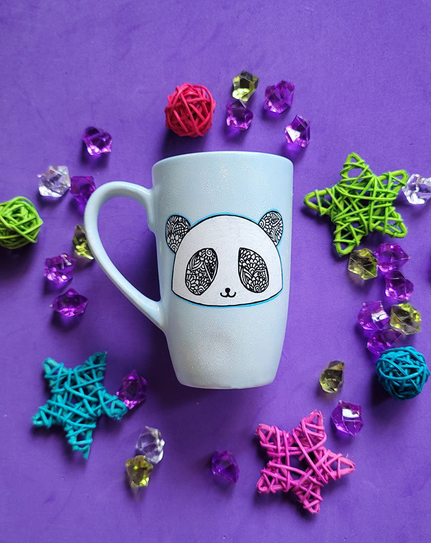 A baby blue hand painted mug with a panda face in zentangles on it