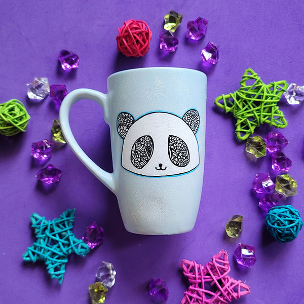 A baby blue hand painted mug with a panda face in zentangles on it