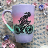 A gradient hand painted mug (lilac-pink-mint-lilac) with a silhouette of a girl on a bike drawn and filled with patterns