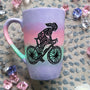 A gradient hand painted mug (lilac-pink-mint-lilac) with a silhouette of a girl on a bike drawn and filled with patterns