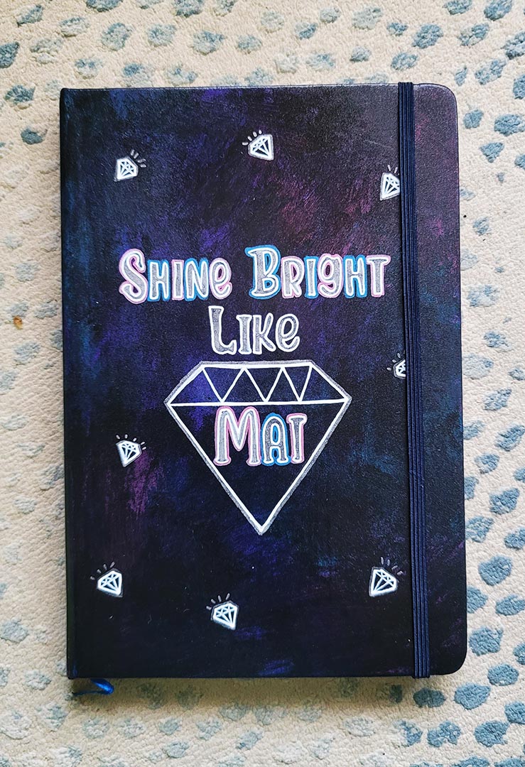 A Dark Sky hand painted notebook with the words shine bright like and a diamond drawn with the name "Mai" inside