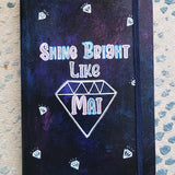 A Dark Sky hand painted notebook with the words shine bright like and a diamond drawn with the name 