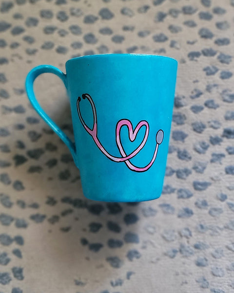 A Light blue mug with a stethoscope painted in pink