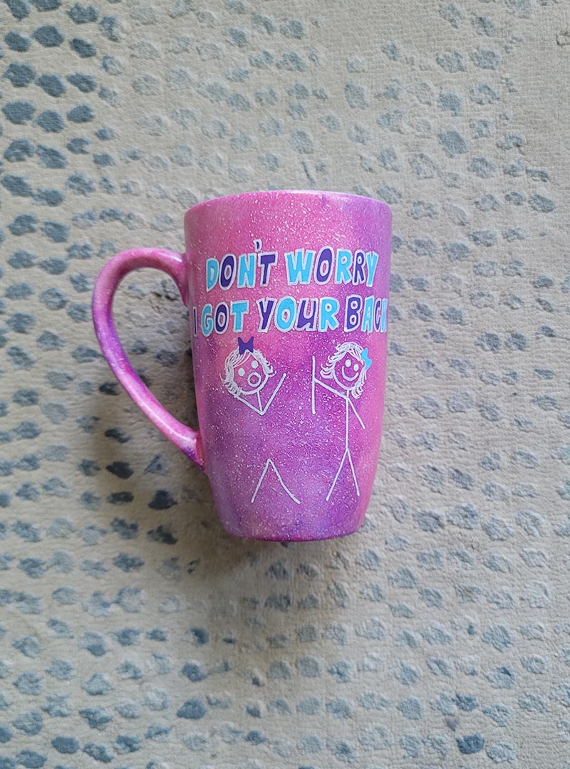 A hand painted pink galaxy mug with the words "don't worry, I got your back " and a drawing of 2 stick figures with the girl holding the back of the other girl