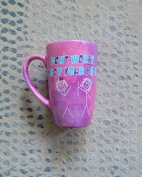 A hand painted pink galaxy mug with the words "don't worry, I got your back " and a drawing of 2 stick figures with the girl holding the back of the other girl