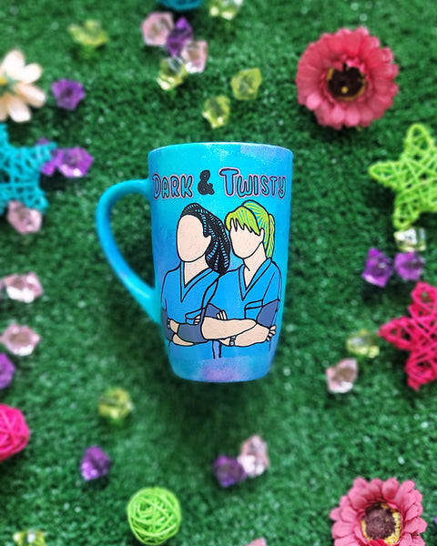 A Blue Hand painted mug with the words "dark and twisty" written on top and a silhouette of 2 girls in medical coats