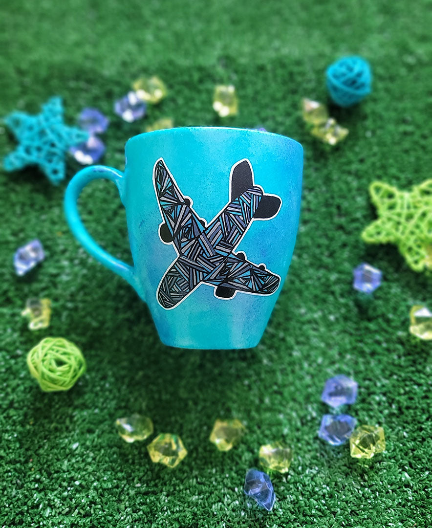 A Blue hand apinted mug with an airplane painted on it full of patterns in grey