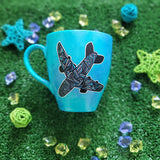 A Blue hand apinted mug with an airplane painted on it full of patterns in grey