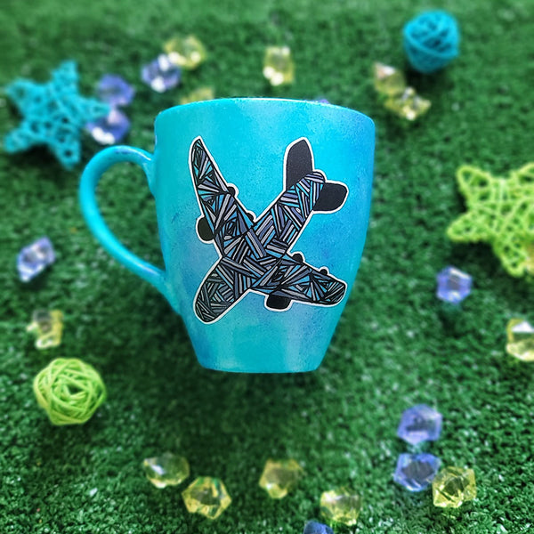 A Blue hand apinted mug with an airplane painted on it full of patterns in grey