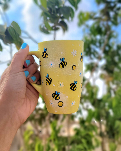 A Pastel yellow Hand painted mug with bees , white flowers and honey combs scattered all over