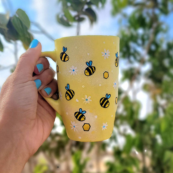 A Pastel yellow Hand painted mug with bees , white flowers and honey combs scattered all over