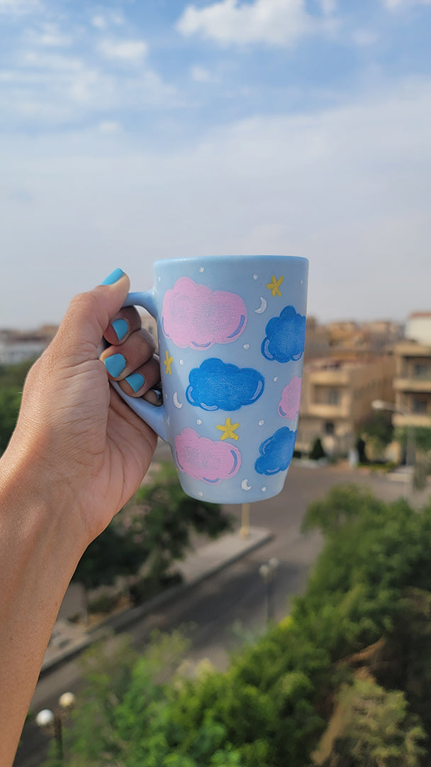 A Baby Blue Hand painted mug with colorful clouds (pink and blue) drawn all over with yellow stars