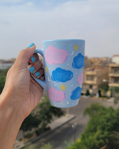 A Baby Blue Hand painted mug with colorful clouds (pink and blue) drawn all over with yellow stars