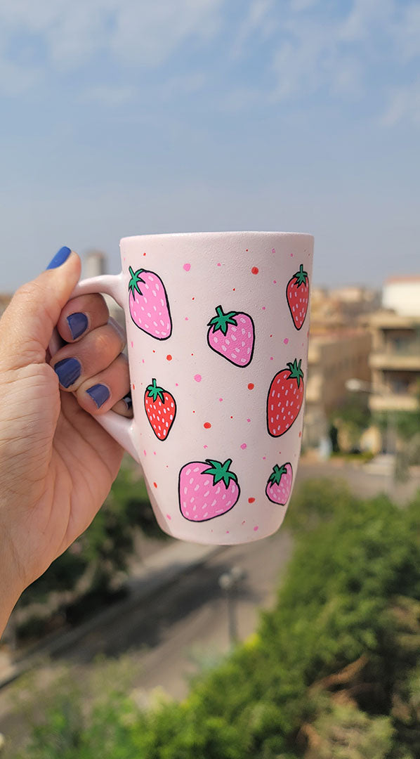 A pastel pink hand painted mug with strawberries in red and pink and red and pink dots, all scattered all over the mug