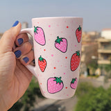 A pastel pink hand painted mug with strawberries in red and pink and red and pink dots, all scattered all over the mug